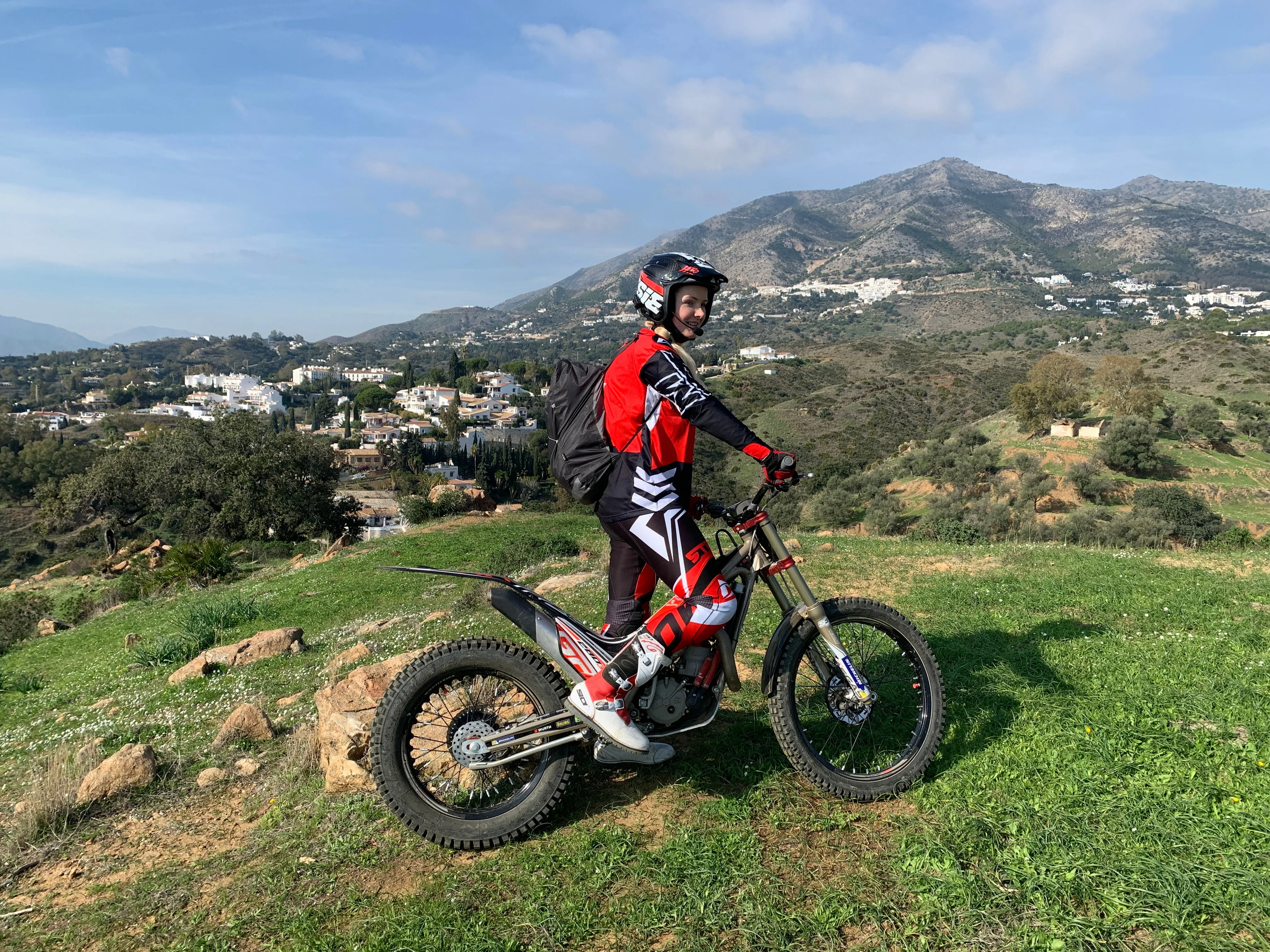 Trialmotorrad auf einer Kuppe, im Hintergrund Berge und weisse Dörfer